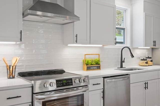 kitchen with appliances with stainless steel finishes, sink, wall chimney exhaust hood, and white cabinets