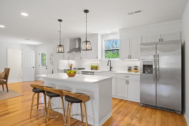 kitchen featuring stainless steel appliances, wall chimney exhaust hood, sink, a kitchen island, and light wood-type flooring