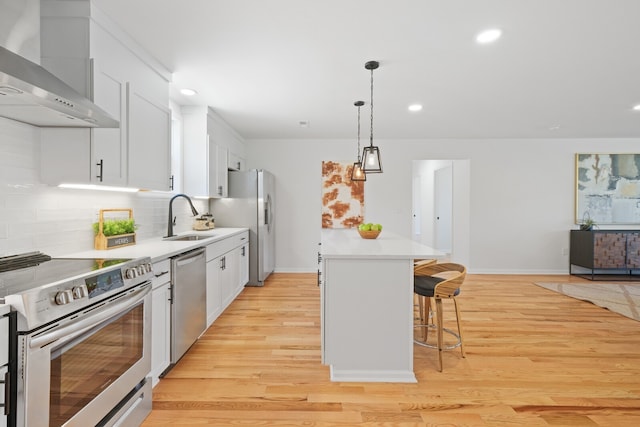 kitchen with light hardwood / wood-style floors, stainless steel appliances, wall chimney exhaust hood, sink, and a kitchen island