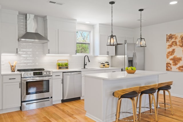 kitchen with stainless steel appliances, light hardwood / wood-style floors, white cabinetry, sink, and wall chimney exhaust hood