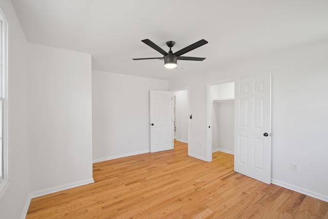 unfurnished bedroom featuring a closet, light wood-type flooring, a spacious closet, and ceiling fan