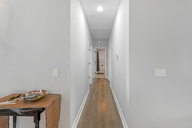 corridor with light wood-type flooring, attic access, and baseboards