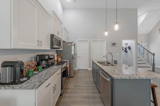 kitchen with wood finished floors, a sink, white cabinetry, appliances with stainless steel finishes, and a center island with sink