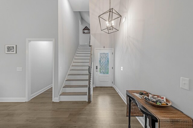 entryway featuring baseboards, a towering ceiling, stairway, wood finished floors, and a chandelier