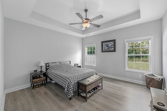 bedroom with ceiling fan, baseboards, a raised ceiling, and wood finished floors