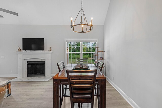 dining area featuring light wood finished floors, baseboards, an inviting chandelier, vaulted ceiling, and a high end fireplace