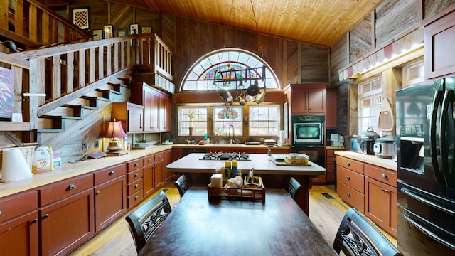 kitchen with black fridge, lofted ceiling, hanging light fixtures, wood walls, and light hardwood / wood-style flooring