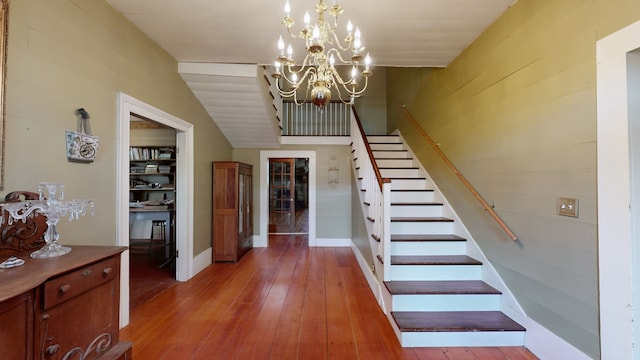 stairs featuring an inviting chandelier, lofted ceiling, and hardwood / wood-style floors