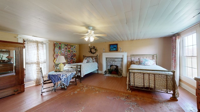 bedroom with hardwood / wood-style flooring, ceiling fan, multiple windows, and a stone fireplace