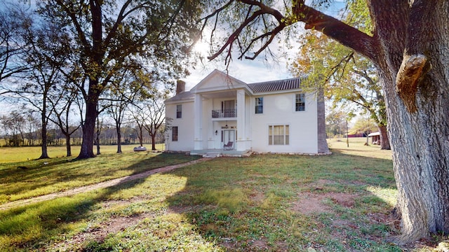 greek revival inspired property featuring a chimney, a front yard, and a balcony