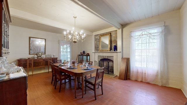 dining area featuring beamed ceiling, a wealth of natural light, wood-type flooring, and an inviting chandelier