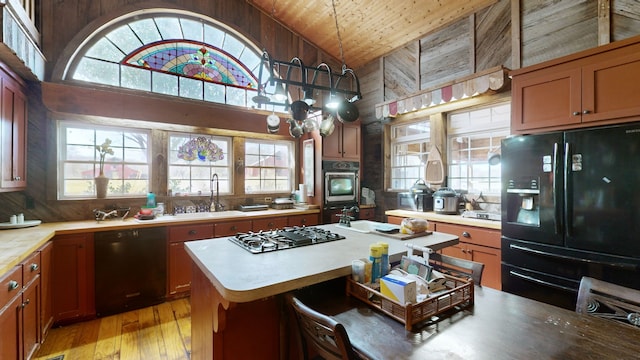 kitchen featuring black appliances, a kitchen island, decorative light fixtures, wooden walls, and sink