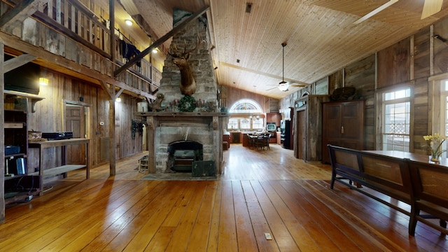 living room featuring a stone fireplace, high vaulted ceiling, wood-type flooring, and ceiling fan