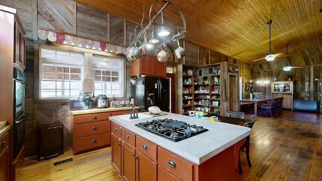 kitchen with light hardwood / wood-style floors, black appliances, high vaulted ceiling, a center island, and wooden walls