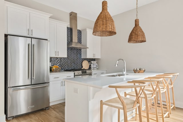 kitchen featuring white cabinetry, a kitchen bar, decorative light fixtures, wall chimney exhaust hood, and appliances with stainless steel finishes