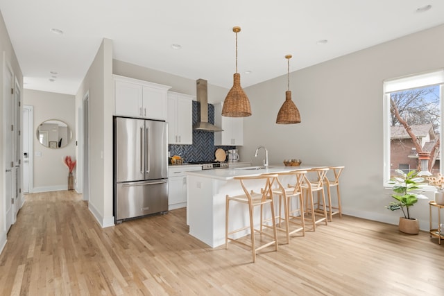 kitchen with light hardwood / wood-style flooring, white cabinetry, wall chimney range hood, high end fridge, and a kitchen breakfast bar