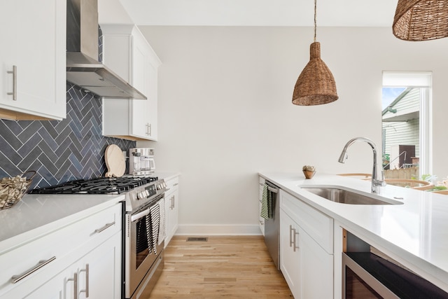 kitchen with white cabinetry, sink, hanging light fixtures, appliances with stainless steel finishes, and wall chimney range hood