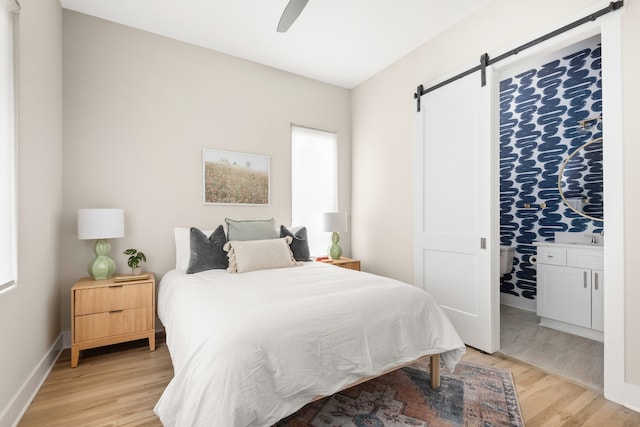 bedroom with a barn door, ceiling fan, and light hardwood / wood-style flooring