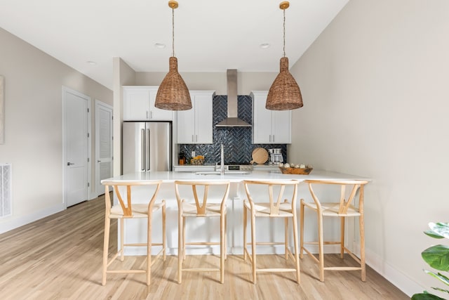 kitchen with light hardwood / wood-style floors, pendant lighting, wall chimney exhaust hood, and stainless steel refrigerator