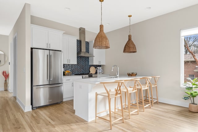 kitchen featuring white cabinets, high end refrigerator, sink, wall chimney exhaust hood, and a kitchen bar