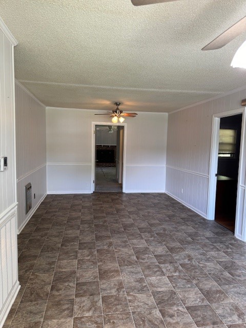 empty room with ceiling fan, a textured ceiling, and wooden walls