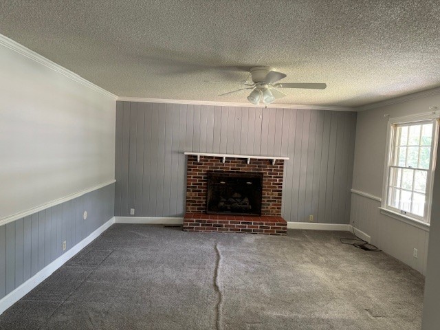 unfurnished living room with ceiling fan, carpet flooring, a fireplace, and ornamental molding