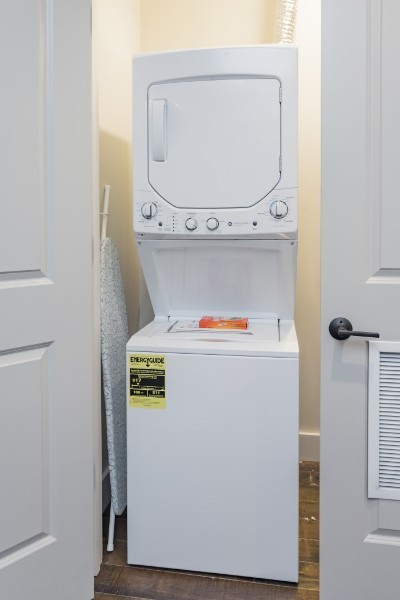 laundry area featuring stacked washing maching and dryer and dark hardwood / wood-style flooring