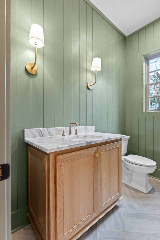 bathroom featuring tile patterned floors, vanity, wood walls, and toilet