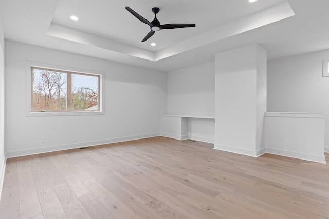 empty room with light hardwood / wood-style floors, ceiling fan, and a tray ceiling