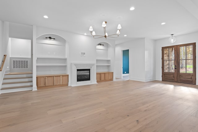 unfurnished living room with a chandelier, french doors, light hardwood / wood-style floors, and built in shelves