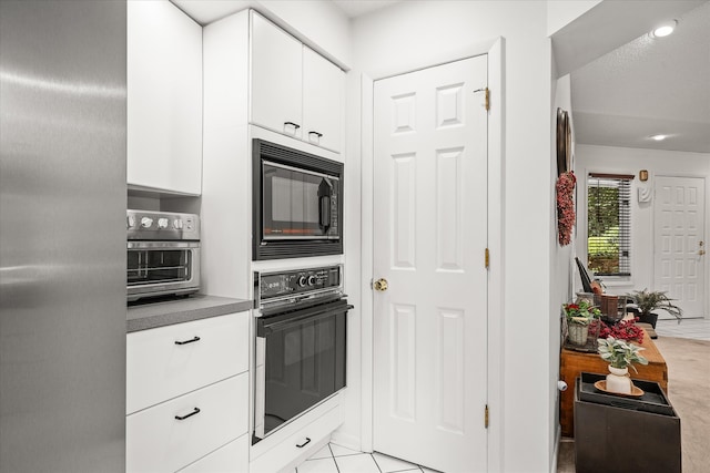 kitchen with black appliances, light tile patterned floors, and white cabinets