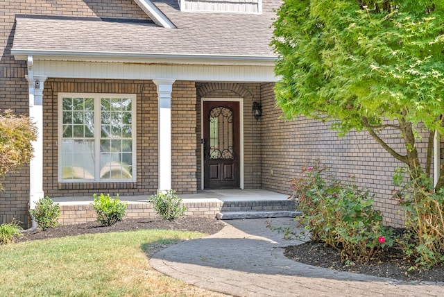 doorway to property with a porch, a shingled roof, and brick siding