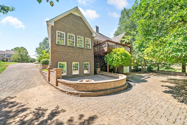 back of property with brick siding, decorative driveway, a chimney, and a wooden deck