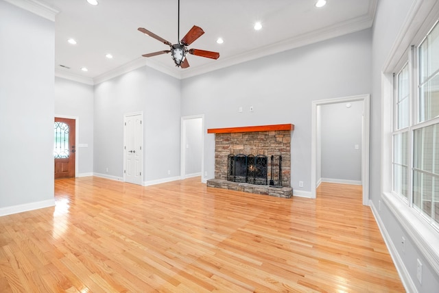 unfurnished living room with a fireplace, a towering ceiling, light wood-style floors, ornamental molding, and baseboards