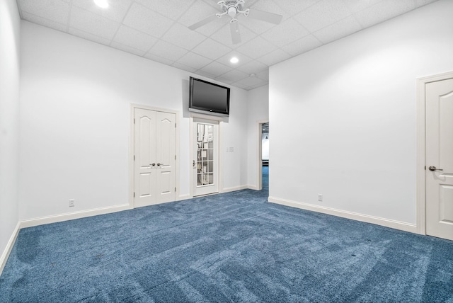 spare room featuring dark colored carpet, a drop ceiling, ceiling fan, and baseboards