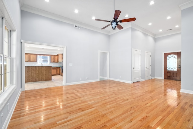 unfurnished living room featuring crown molding, a towering ceiling, ceiling fan, and light hardwood / wood-style floors