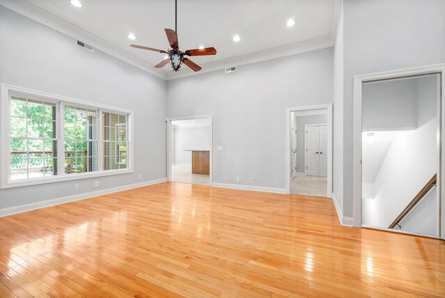 unfurnished living room featuring light hardwood / wood-style flooring, ceiling fan, ornamental molding, and a towering ceiling