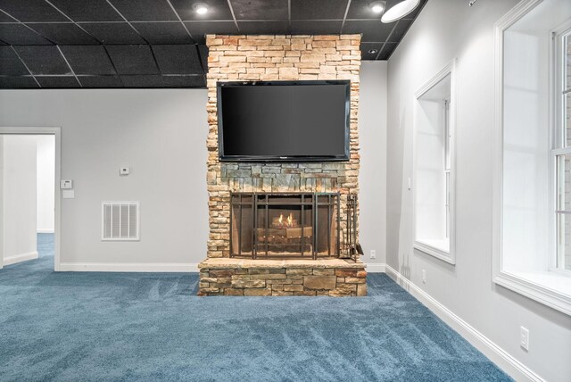 unfurnished living room featuring carpet, a drop ceiling, and a stone fireplace