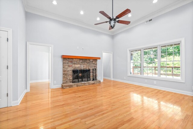 unfurnished living room with crown molding, ceiling fan, a stone fireplace, and light wood-type flooring