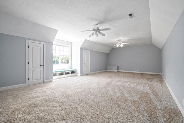 additional living space with ceiling fan, a textured ceiling, light carpet, and vaulted ceiling