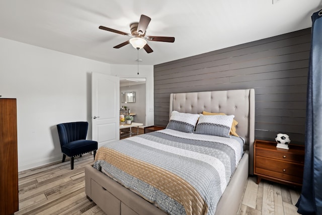 bedroom featuring light wood-type flooring, ceiling fan, and wooden walls