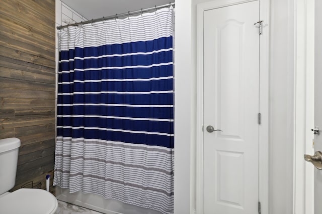 bathroom featuring toilet, wood walls, and shower / bathtub combination with curtain