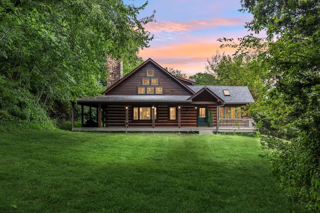 back house at dusk featuring a yard and covered porch