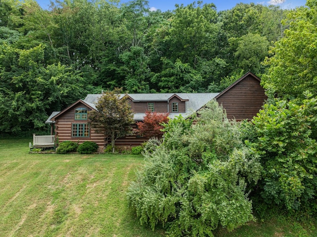 exterior space with a front lawn, a wooden deck, and a view of trees