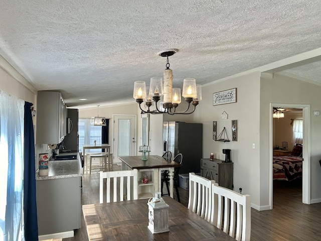 dining area featuring a chandelier, a textured ceiling, vaulted ceiling, ornamental molding, and dark wood finished floors