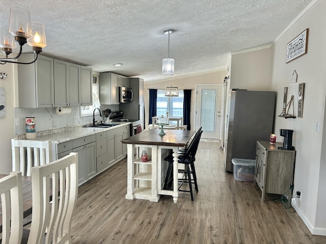 kitchen with stainless steel appliances, a sink, wood finished floors, vaulted ceiling, and gray cabinets