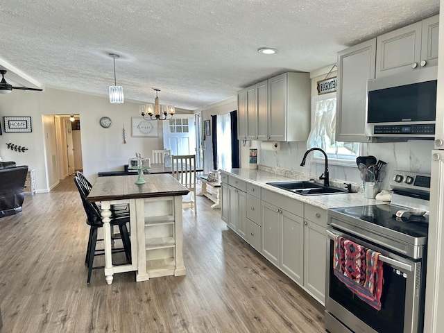 kitchen with ceiling fan with notable chandelier, wood finished floors, a sink, vaulted ceiling, and appliances with stainless steel finishes