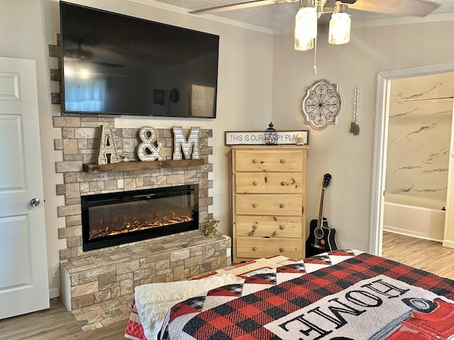 bedroom featuring wood finished floors, ensuite bathroom, a stone fireplace, crown molding, and a textured ceiling