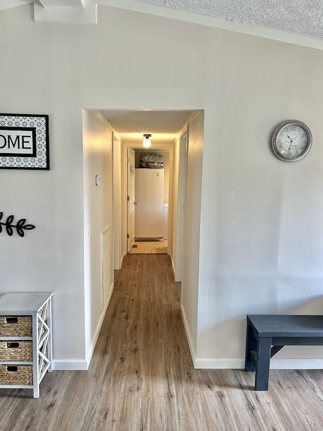 hall featuring a textured ceiling, baseboards, and wood finished floors