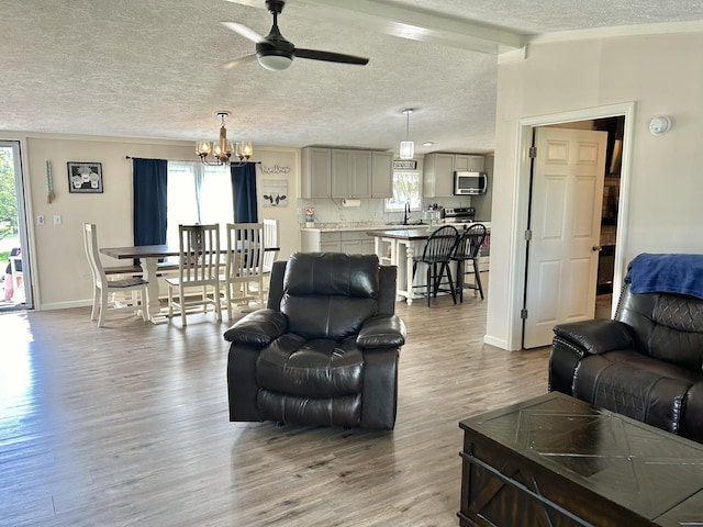 living room featuring vaulted ceiling with beams, a textured ceiling, wood finished floors, baseboards, and ceiling fan with notable chandelier